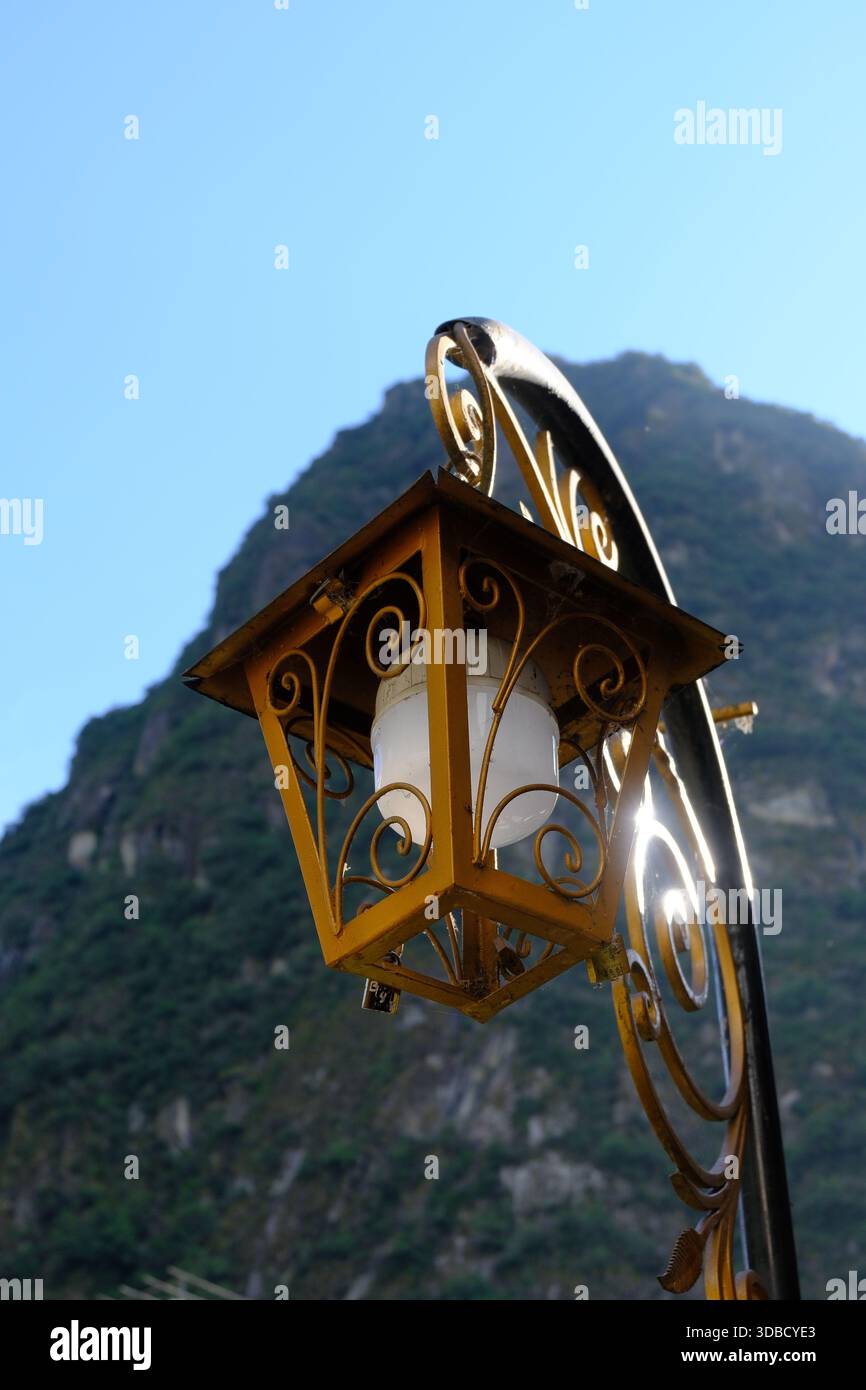 Dekorative Straßenlaterne in Machu Picchu Pueblo mit sonnendurchfluteten Andenbergen im Hintergrund, Peru Stockfoto