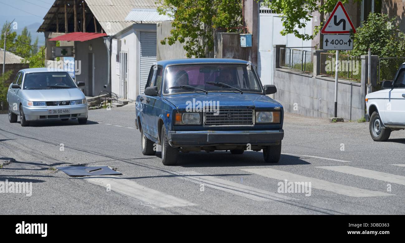 Ein blaues Auto auf einer Stadtstraße, umgeben von Straßenschildern an einem sonnigen Tag, Lada 2107, auch WAS-2107, VAZ-2107, Lada Nova oder Lada Riva fährt ohne Lizenz Stockfoto