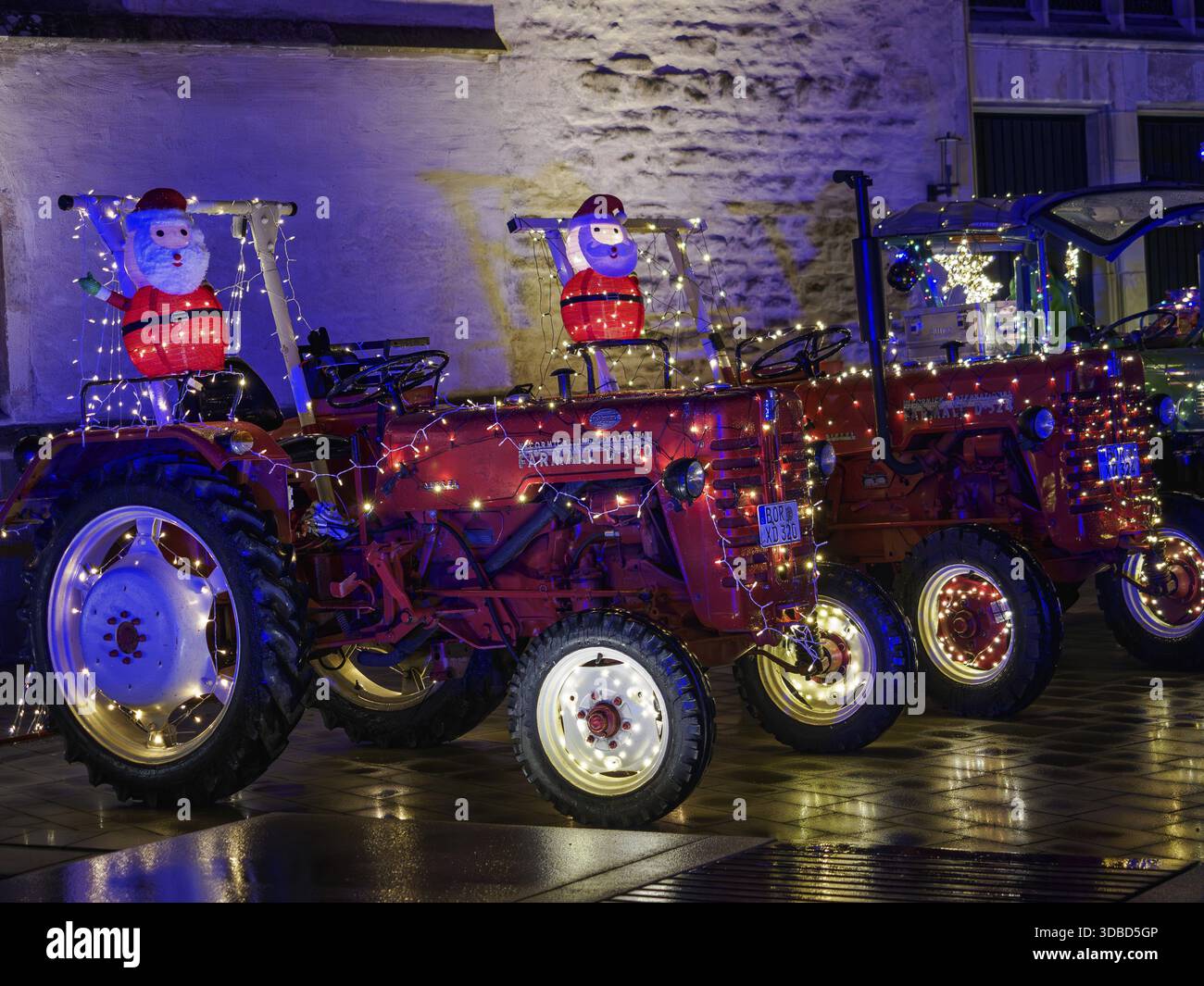 Rote Traktoren mit Weihnachtsbeleuchtung und Weihnachtsmannsfiguren bei Nacht, Borken, Münsterland, Deutschland Stockfoto