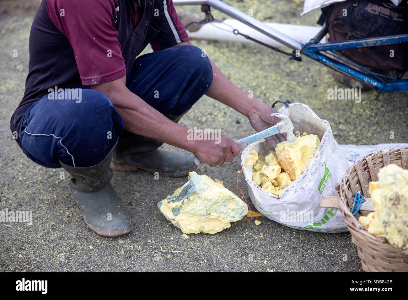 Der Schwefelminer zerlegt seine Schwefelladung in kleinere Stücke, bevor er sie in Körbe transportiert, Kawah Ijen Vulkan, Java, Indonesien Stockfoto