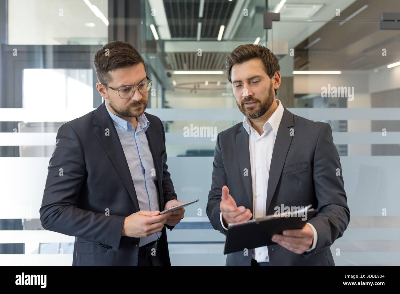 Zwei professionelle Geschäftsleute arbeiten in einem modernen Büro zusammen und analysieren Dokumente und führen eine konzentrierte Diskussion über strategische Geschäftsentwicklung und Partnerschaft Stockfoto