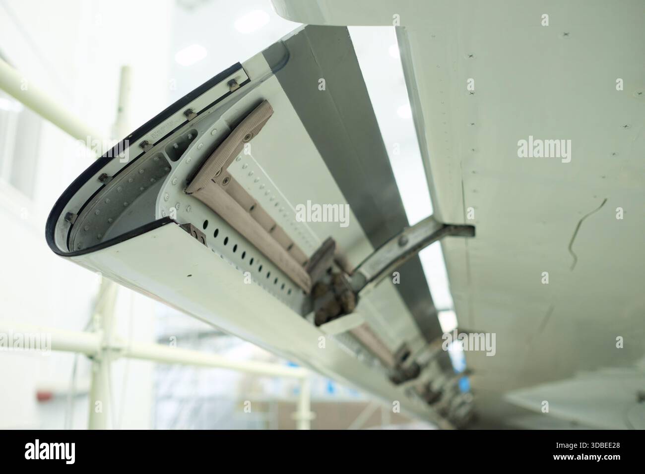 Nahaufnahme eines Flugzeugflügelklappenmechanismus in einer Instandhaltungseinrichtung. Werkzeuge und Ausrüstung sind sichtbar, was die komplizierte Konstruktion unterstreicht Stockfoto