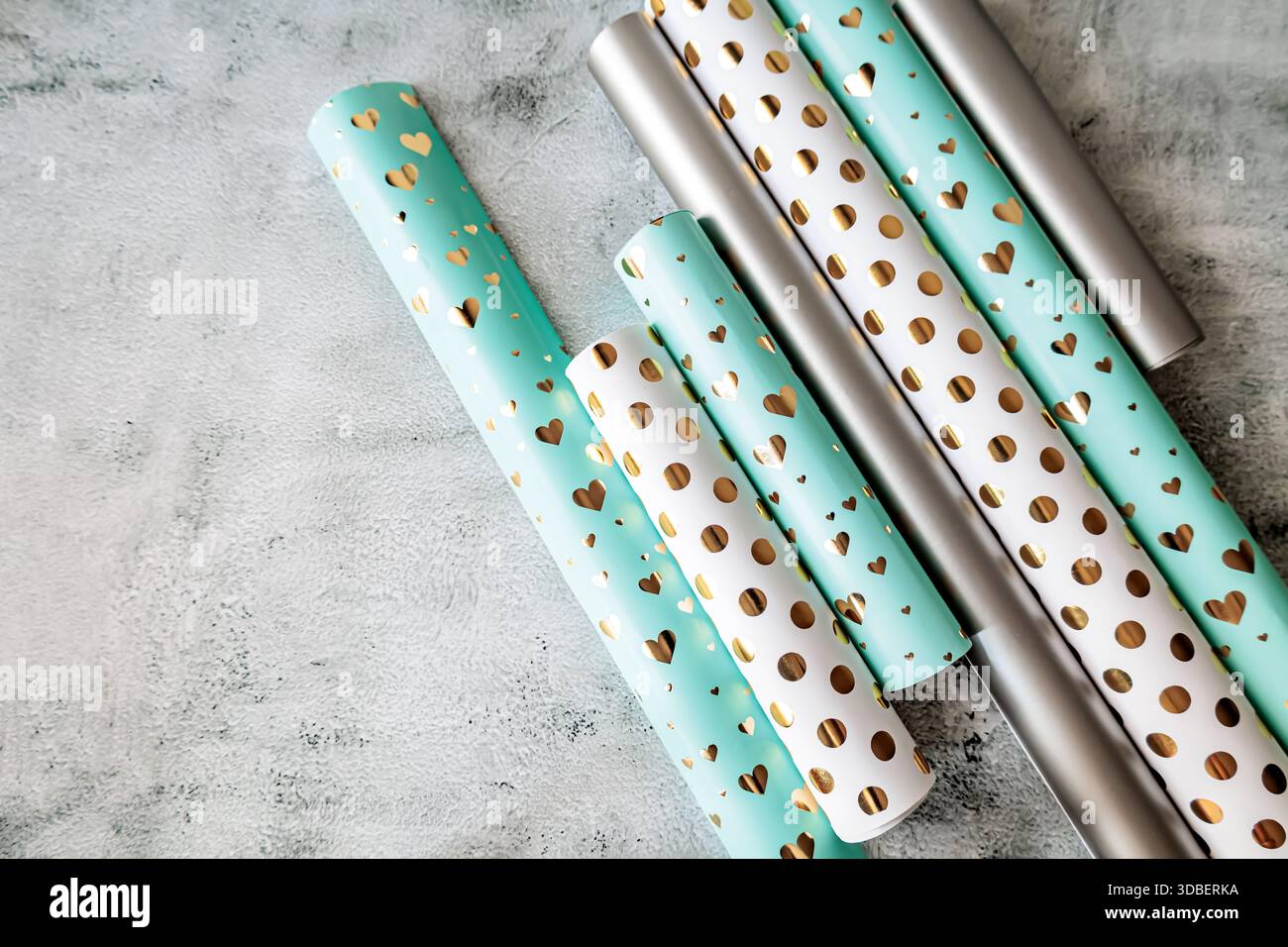 Draufsicht auf Geschenkpapier in weichen Pastellfarben und glänzenden goldenen Prints. Festliche Papierrollen für Verpackungs-, Bastel- und Urlaubsdesign Stockfoto