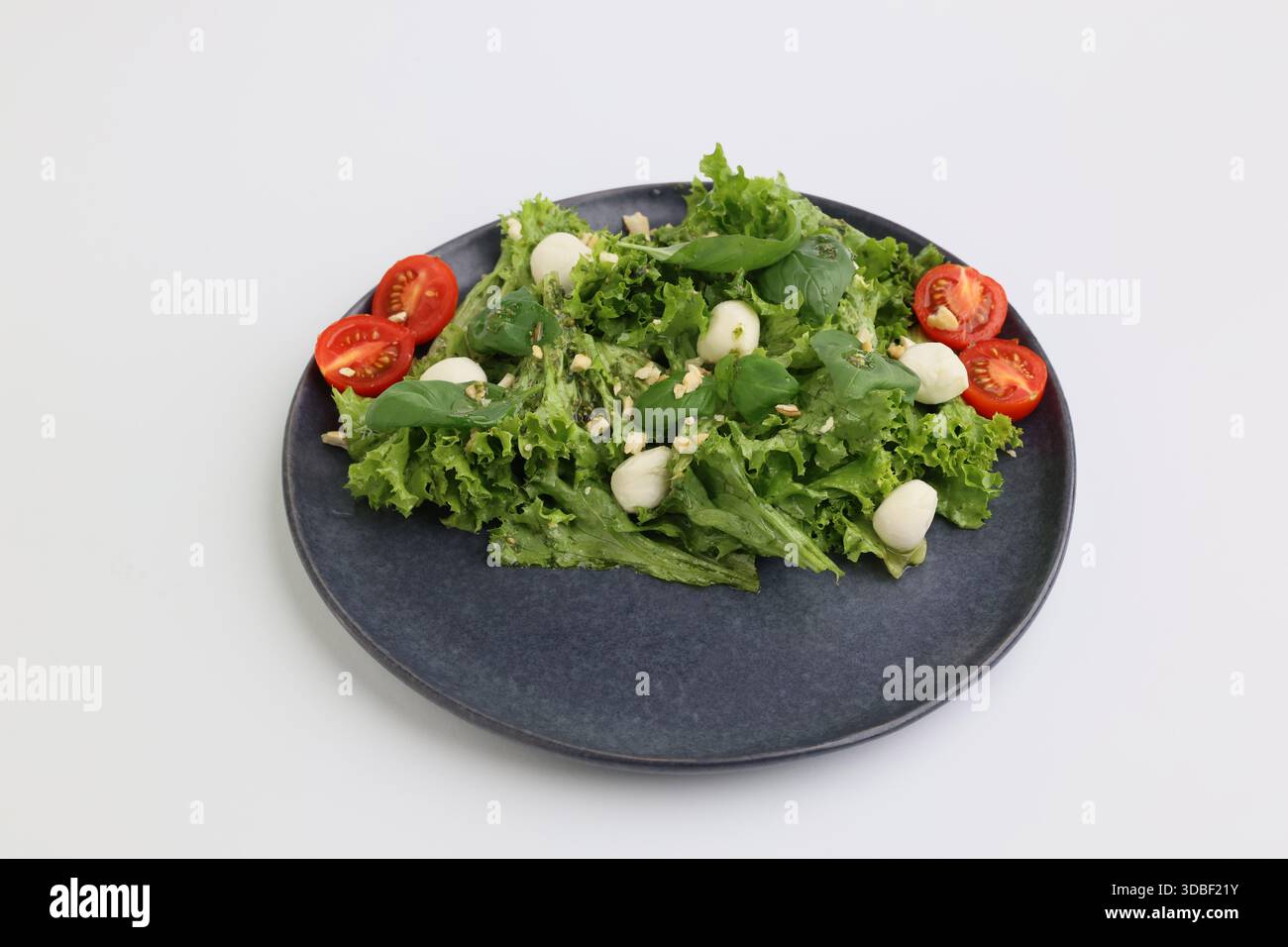 Sommerfrischer Diätsalat mit Kirschtomaten, Mozzarella, Basilikum und Olivenöl auf dunkler Platte auf weißem Hintergrund. Gesundes Mittagessen. Stockfoto