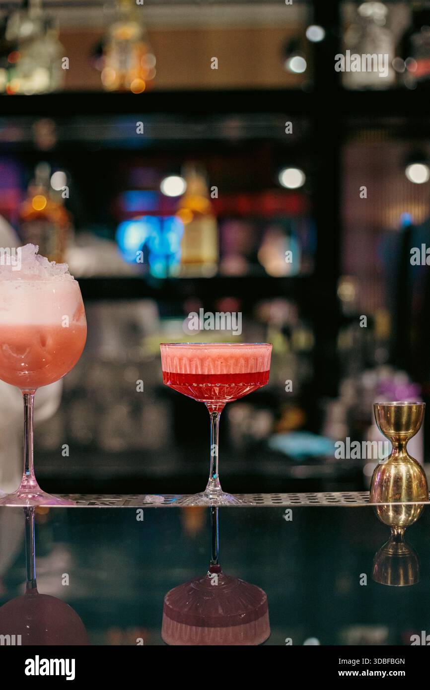 Stilvolle Nahaufnahme zweier roter Cocktails in Stielgläsern auf einer modernen Bartheke mit Schaum-, Zitrusgarnitur und stimmungsvoller Atmosphäre im Nachtleben Stockfoto