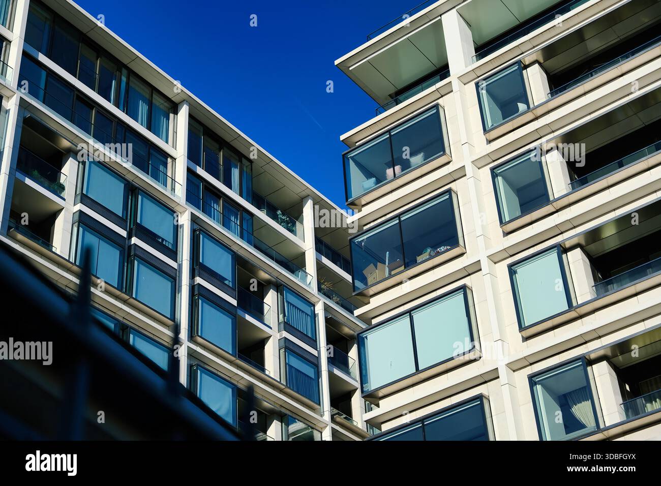 Modernes Luxus-Apartment-Gebäude mit Glasbalkonen und großen reflektierenden Fenstern vor klarem blauem Himmel in urbaner Umgebung Stockfoto