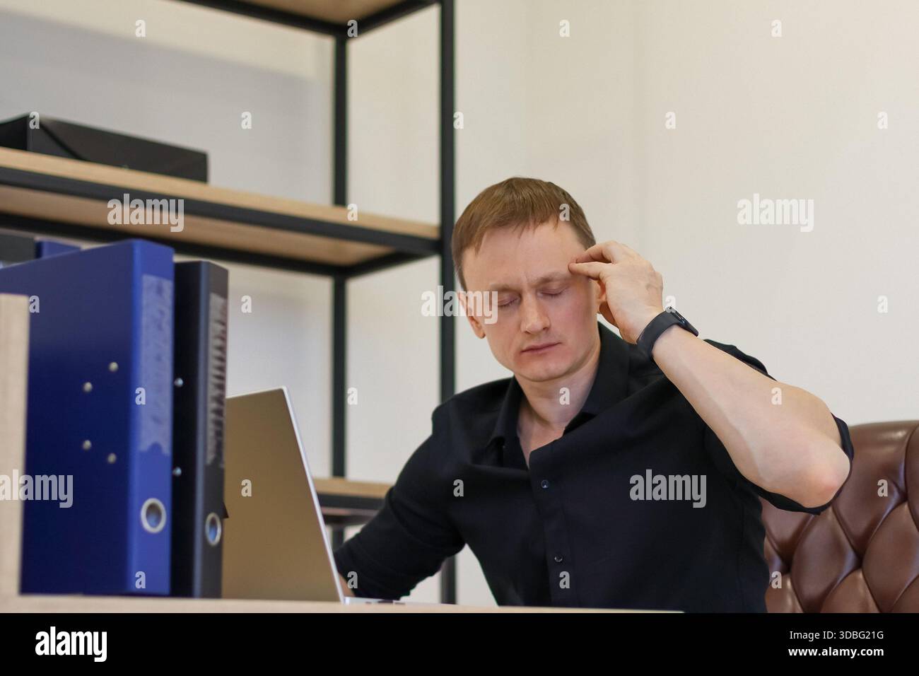 Junger Mann in schwarzem Hemd am Schreibtisch mit Ordnern, Handpressung des Tempels bei Stress oder Müdigkeit Stockfoto