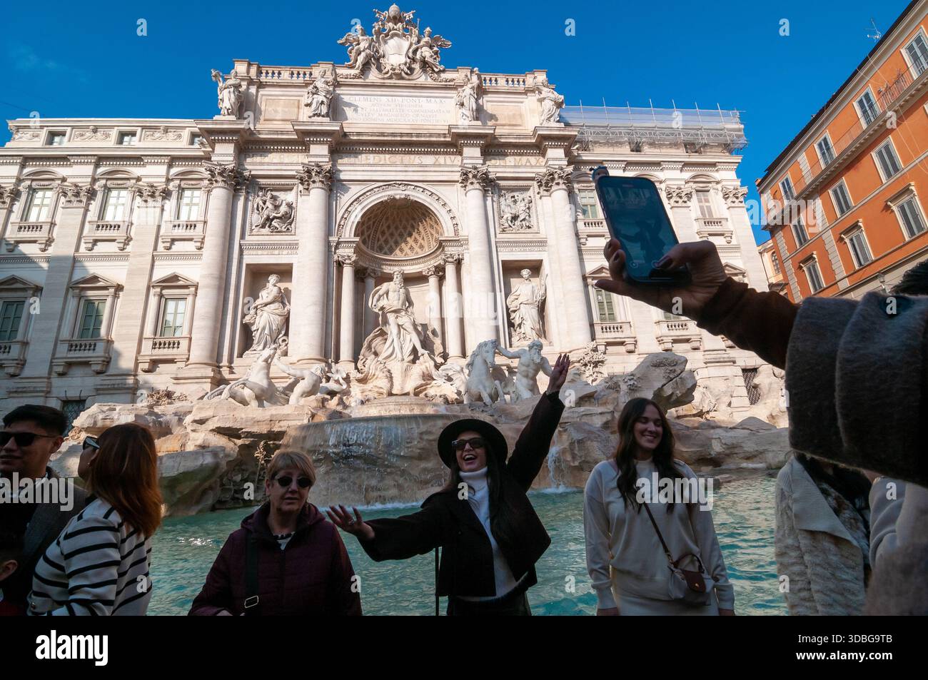 Ein Touristenmädchen mit Hut posiert vor dem Trevi-Brunnen für ein Smartphone-Foto in Rom. Stockfoto