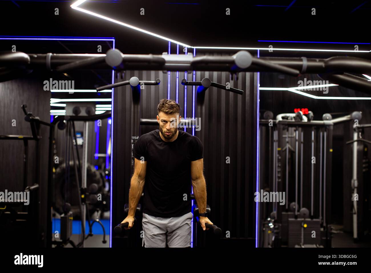 Der Mann übt Krafttraining in einem eleganten Fitnessstudio und betont Fokus und Entschlossenheit in dynamischer Beleuchtung. Stockfoto