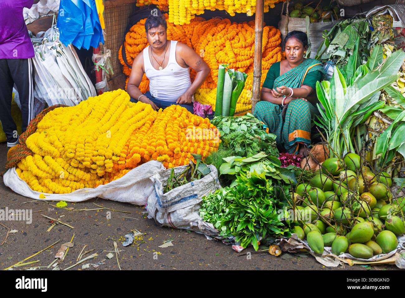 Zwei Stände auf dem Blumenmarkt in Kalkutta, an denen Ringelblumengirlanden und Gemüse verkauft werden Stockfoto