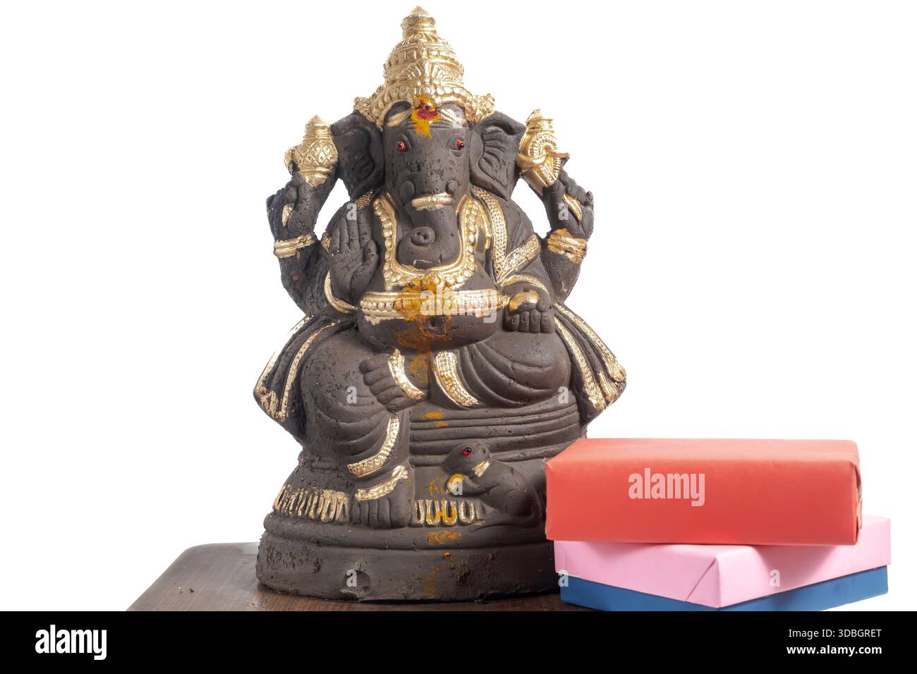 Ein handgefertigtes Ganesha-Idol aus Lehm, das auf einem Holztisch zusammen mit einer Geschenkbox vor einem sauberen weißen Hintergrund platziert wird. Perfekt für Festivalthemen, spi Stockfoto