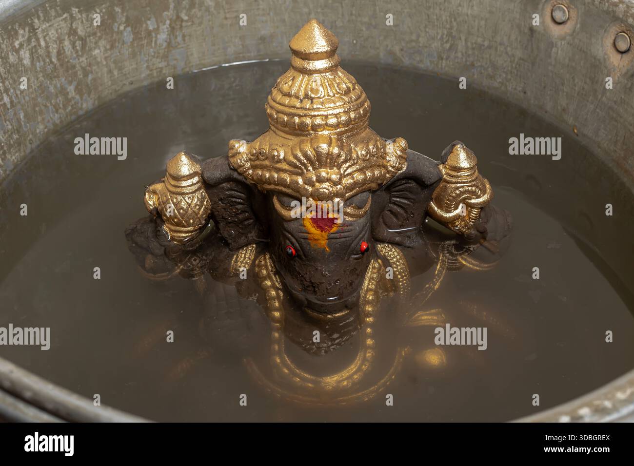 Ein goldenes Ganesha-Idol, das während des Ganesh Chaturthi-Rituals in Wasser getaucht ist und die traditionelle Hindufestszene einfängt. Stockfoto
