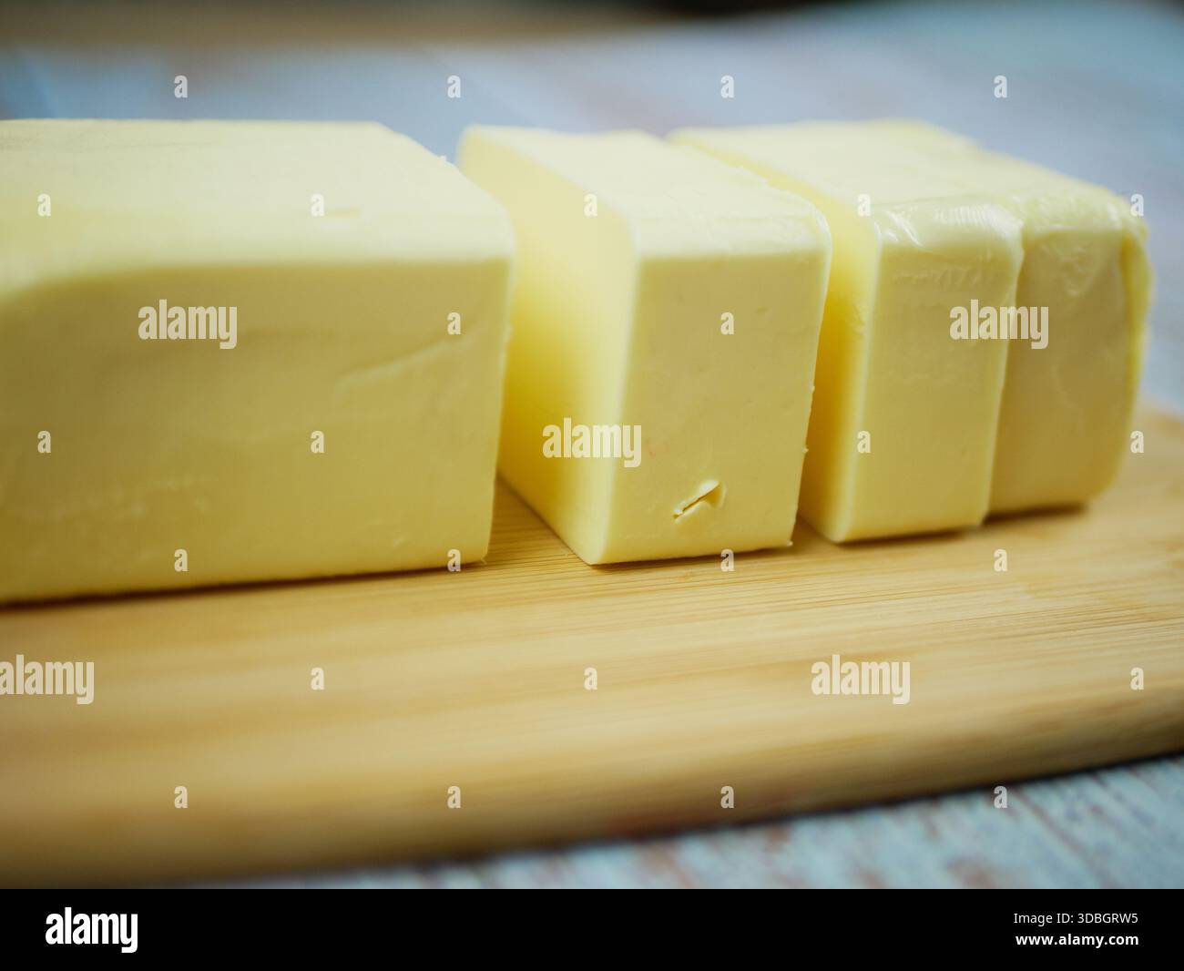 Geschnittener Butterblock in gleiche Portionen auf hölzernem Schneidebrett schneiden – Close-up Frische Milchzutat zum Backen und Kochen Stockfoto