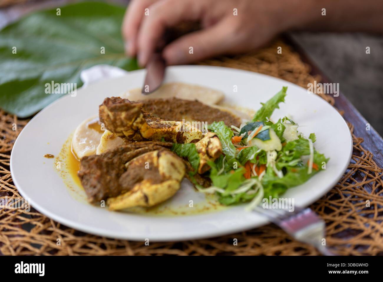 Currykrabben und Knödel serviert auf einem weißen Teller, ein traditionelles Tobago-Gericht, das karibische Aromen und die kulinarische Kultur der Insel hervorhebt. Stockfoto
