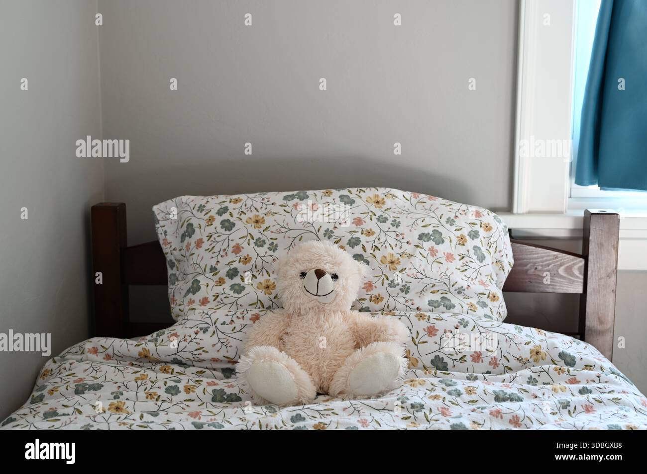 Ein weicher Teddybär sitzt auf einem Bett mit zartem Blumenmuster und sorgt so für eine warme und gemütliche Atmosphäre. Sanfte Pastellfarben. Stockfoto