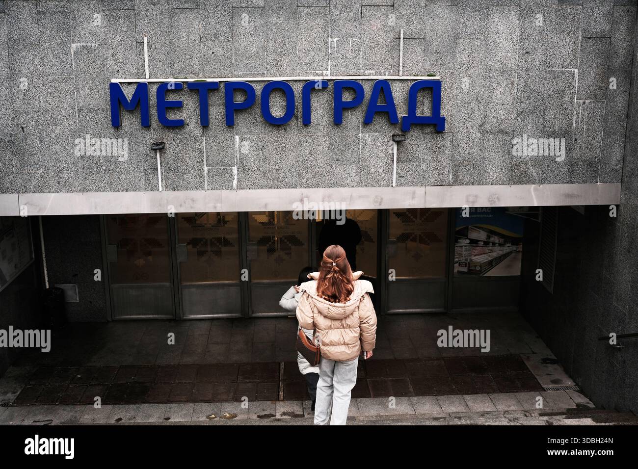 Eine Person nähert sich dem Eingang einer modernen U-Bahn-Station in einem pulsierenden Stadtgebiet. Metrograd. Kiew, Ukraine. Dezember 2025. Stockfoto