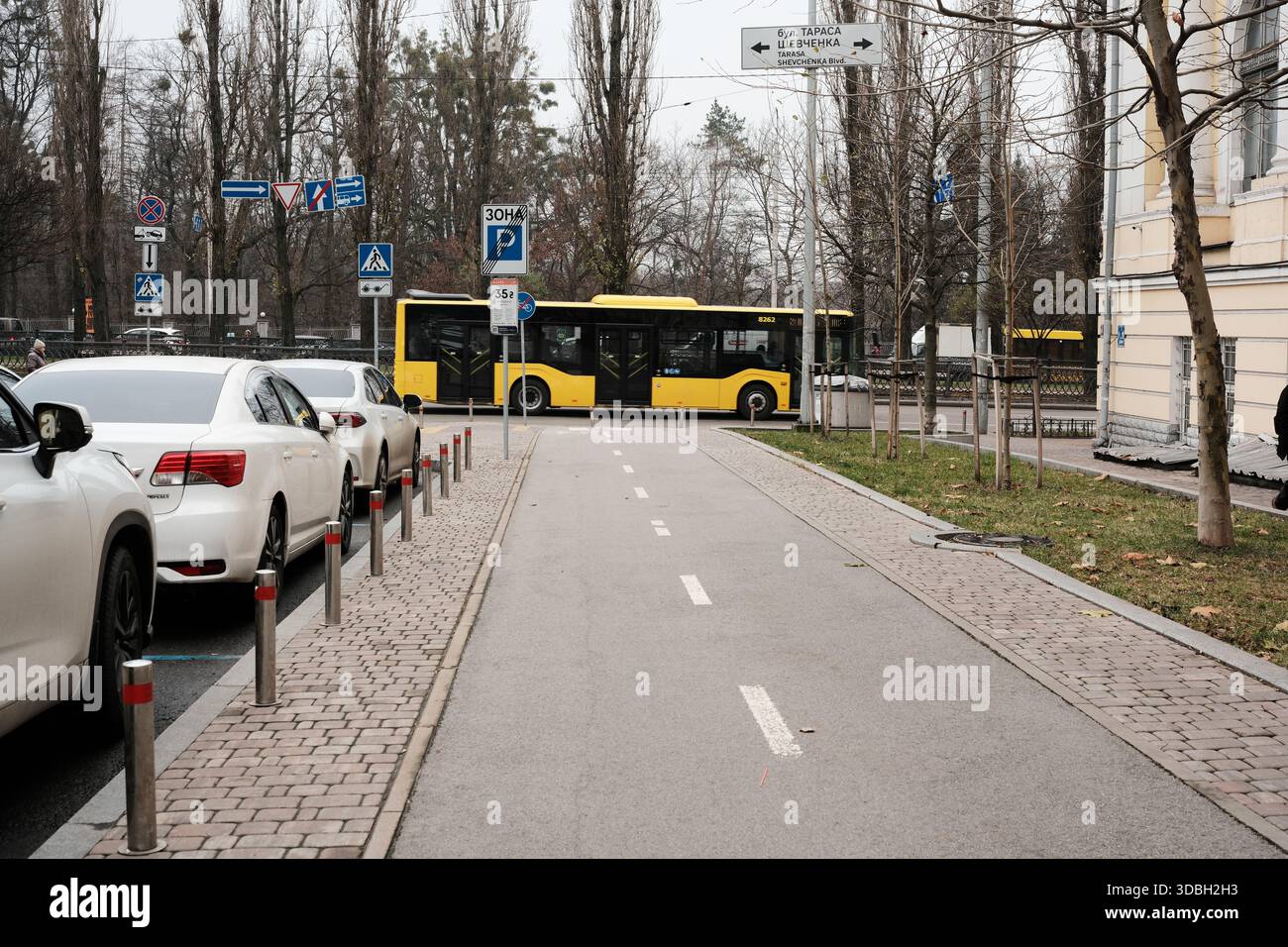 Eine geschäftige Stadtszene zeigt einen gelben Bus, der bei grauem Wetter an geparkten Autos vorbeifährt. Shevchenko Boulevard. Kiew, Ukraine. Dezember 2025. Stockfoto