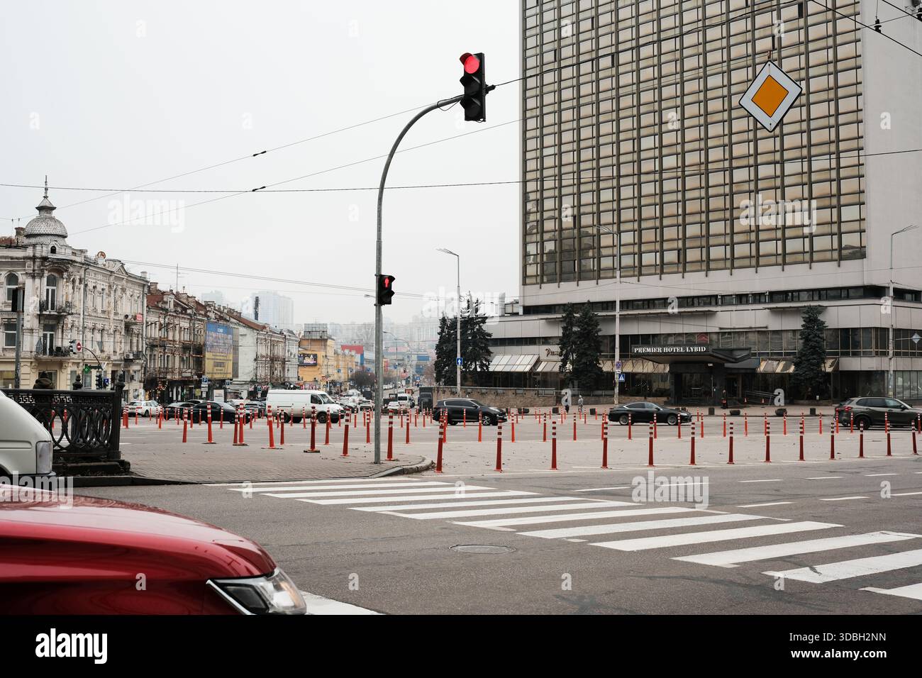 Autos warten an einem bewölkten Tag an einer Ampel in der Nähe eines hohen Gebäudes. Kiew, Ukraine. Dezember 2025. Stockfoto