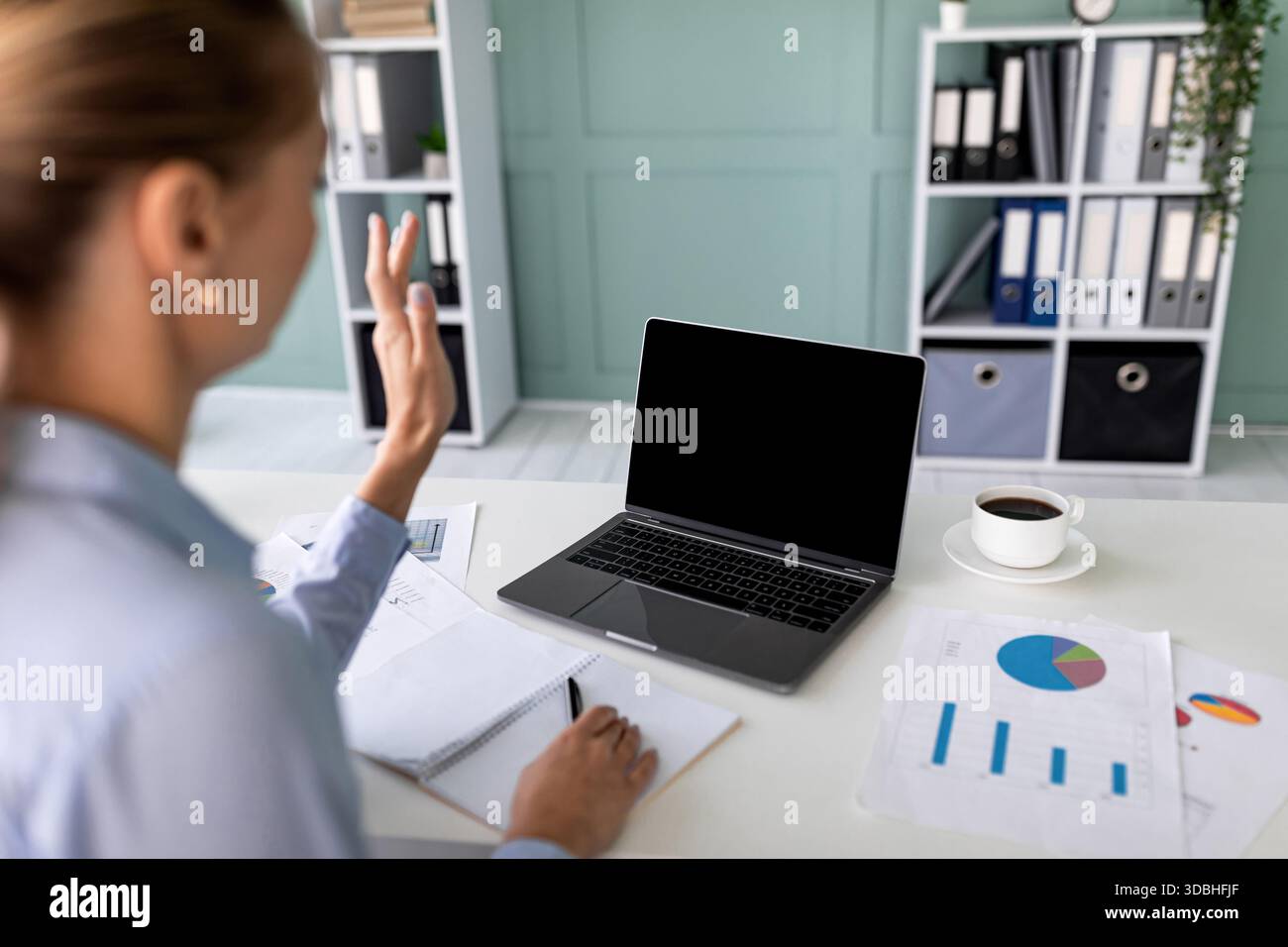 Geschäftsfrau nimmt Remote Meeting Teil, während sie vom Home Office aus arbeitet und der Webcam zuwinkt Stockfoto
