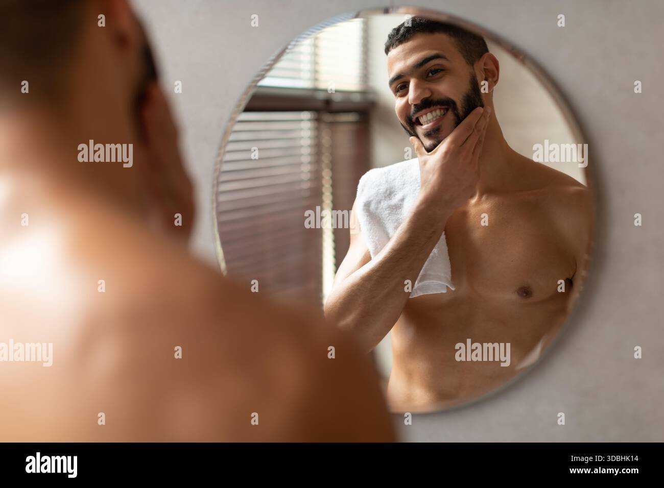 Selbstbewusster junger arabischer Mann, der morgens die Hautpflege-Routine im modernen Badezimmer genießt Stockfoto