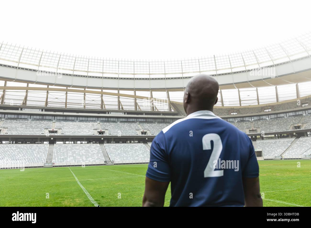Fußballspieler, der auf dem grünen Rasenfeld im modernen Stadion steht, trägt blaues Trikot 2. Backview, Pregame, Antizipation, Arena, Tribüne, Außenbereich, Stockfoto