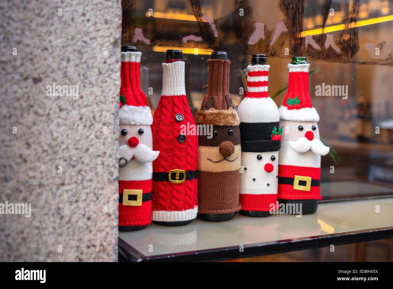 Eine festliche Ausstellung von Weinflaschen mit Strickbezügen im Weihnachtsmotiv, mit Weihnachtsmann, Rentier und Schneemann, die Weihnachten spi zeigen Stockfoto