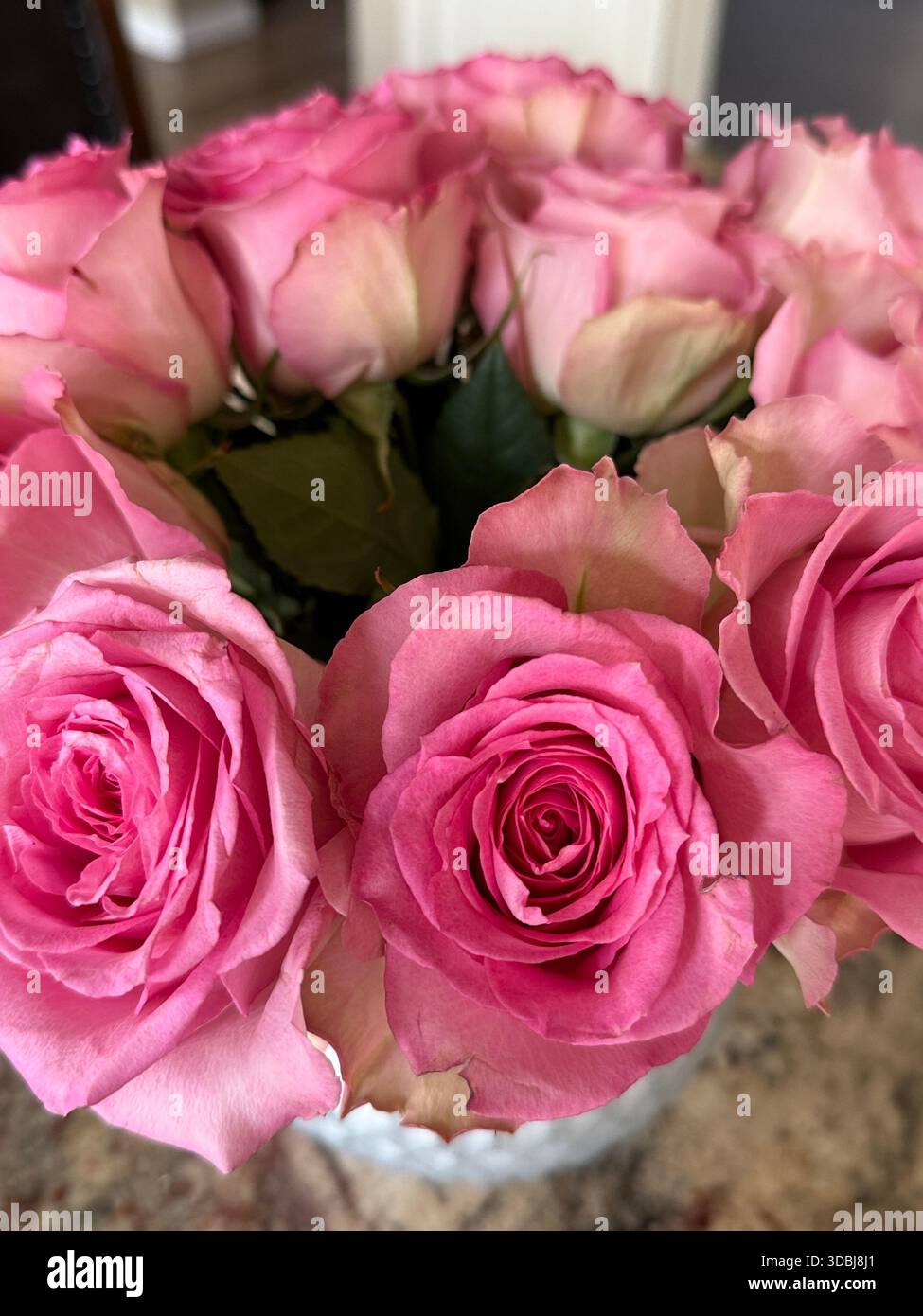 Üppige Arrangements von leuchtend rosa Rosen in einer Glasvase, kombiniert mit pfirsichfarbenen Rosen für eine volle, romantische und elegante Blumendekoration. Stockfoto