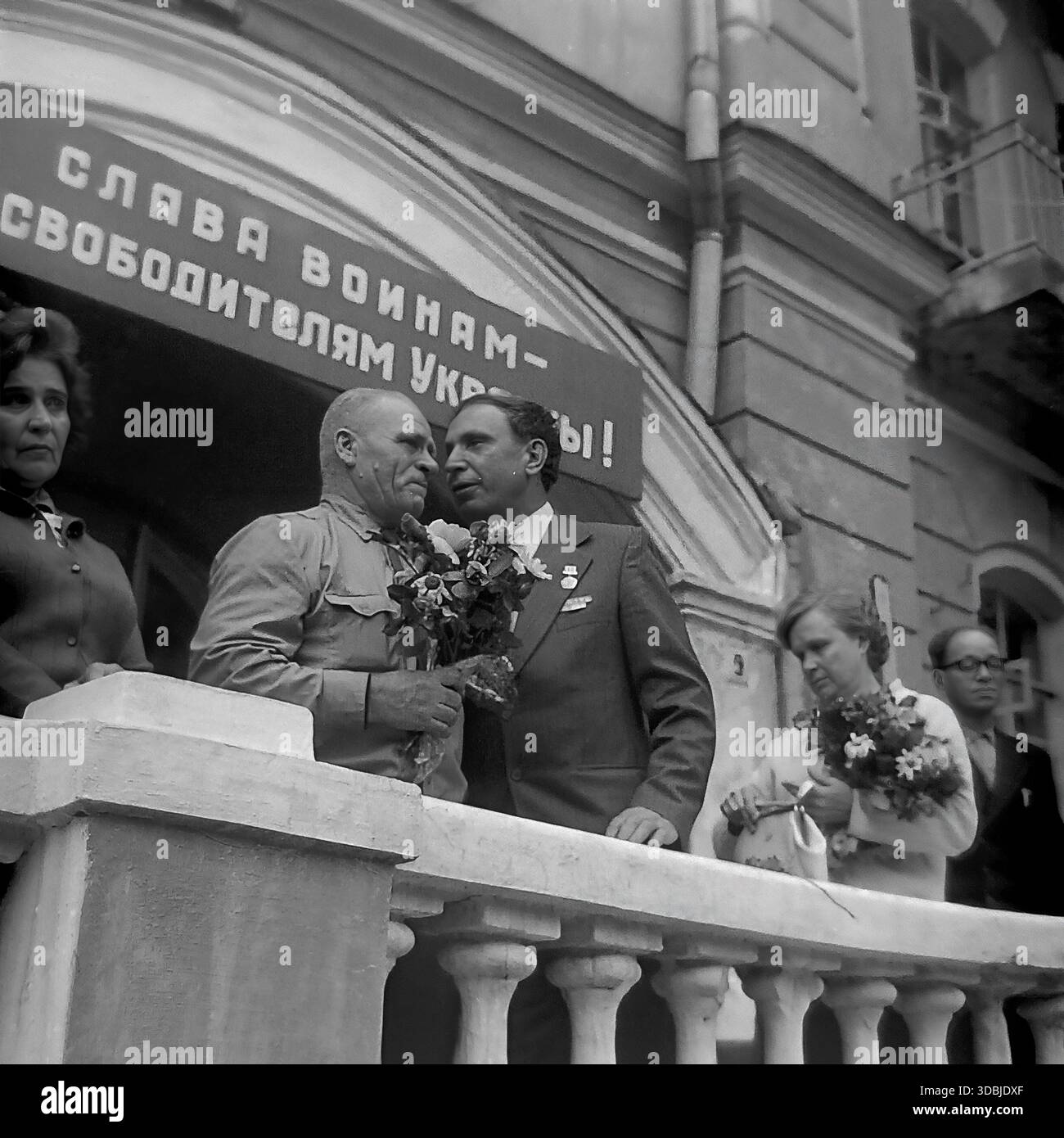 September 1978. Slavyanogorsk (jetzt Sviatohirsk), Region Donezk, Ukrainische SSR, UdSSR. Ein emotionales Treffen zwischen dem blinden Kriegsheld Shutenko und einem Kameraden in einer SoldatenTunika auf dem Balkon eines Gebäudes. Die Veteranen umarmen und küssen sich während einer Kundgebung zum 35. Jahrestag der Befreiung der Ukraine. Oben steht ein Banner mit der Aufschrift 'Ruhm an die Krieger-Befreier!'. Authentisches Archivbild, das die Atmosphäre der Bruderschaft und des friedlichen Lebens im sowjetischen Donbass feststellt. Stockfoto