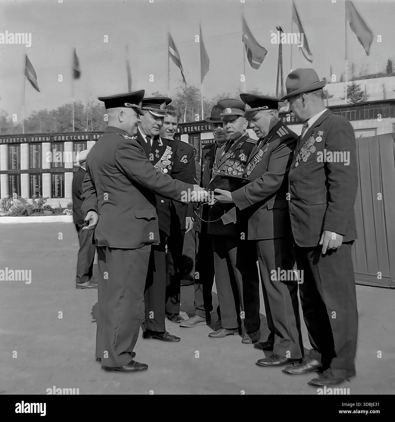 September 1978. Dorf Dolina, Bezirk Sloviansk, Region Donezk, ukrainische SSR, UdSSR. Während des 35. Jahrestages der Befreiung des Dorfes von der Nazi-Besatzung versammeln sich in der Nähe der Gedenkmauer eine Gruppe dekorierter Veteranen des Zweiten Weltkriegs, darunter Militäroffiziere und Zivilisten. Die Kameraden untersuchen ein Erinnerungsalbum, während sie unter Fahnen stehen. Authentisches Archivbild, das die Atmosphäre der Brüderlichkeit, des Patriotismus und des friedlichen Lebens im sowjetischen Donbass während der Breschnew-Ära feststellt. Stockfoto
