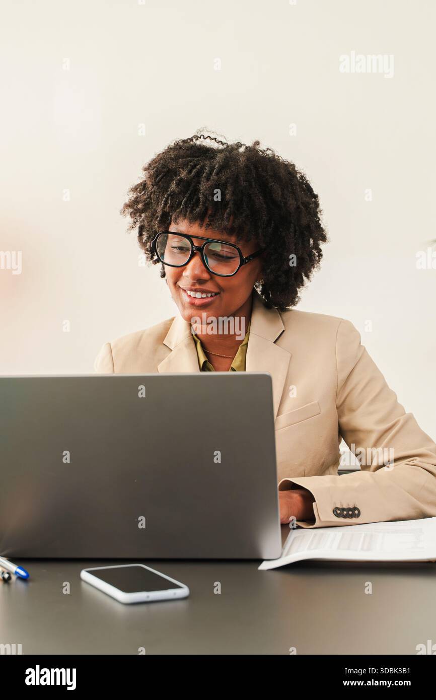Eine professionelle Frau arbeitet in einem maßgeschneiderten Anzug an ihrem Laptop und zeigt Konzentration und Hingabe an ihrem Schreibtisch, verkörpert sie Stockfoto