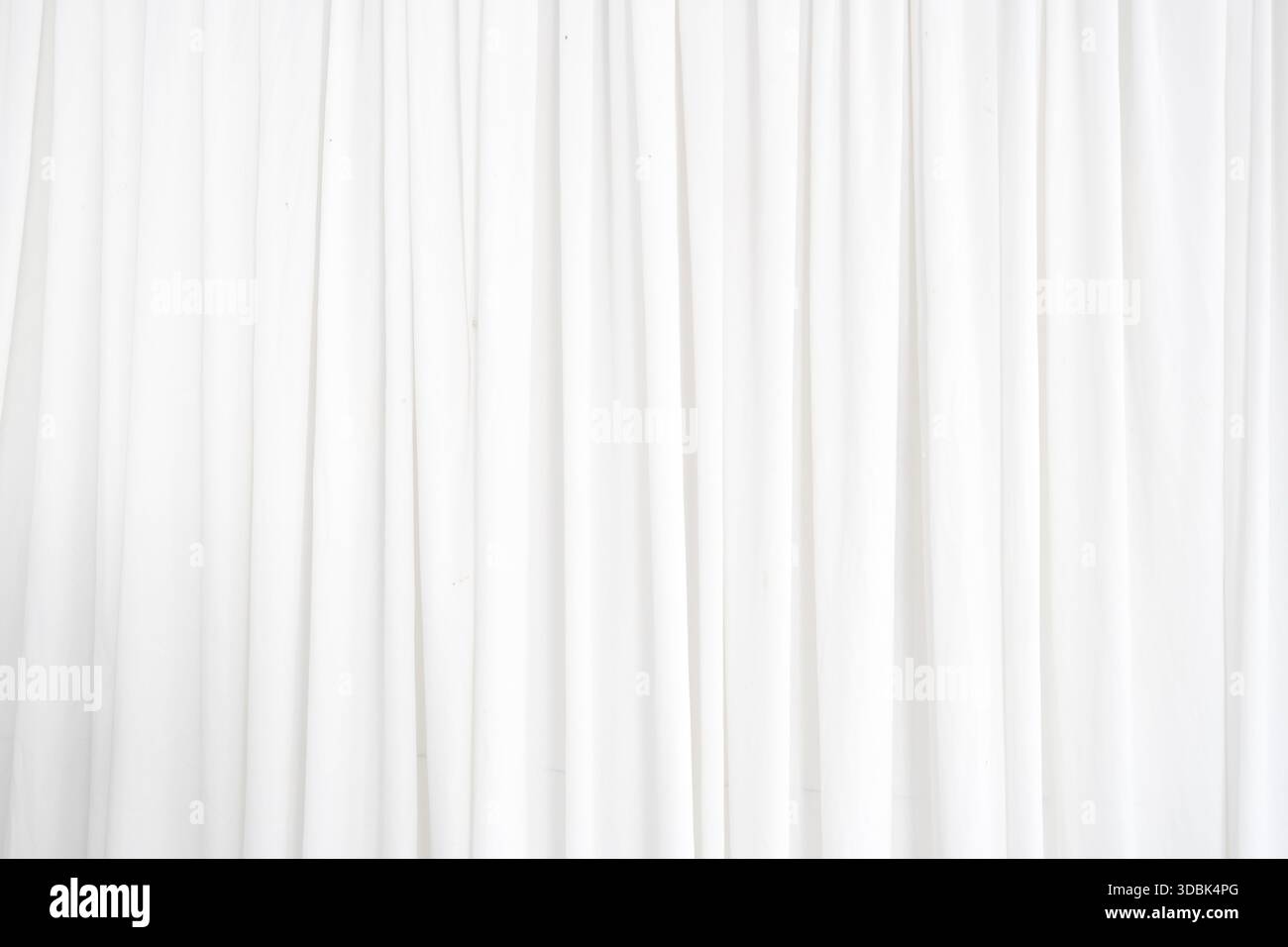 Ein langer weißer Vorhang hängt vor einem weißen Hintergrund. Der Vorhang besteht aus einem transparenten Material, das Licht durchlässt. Der Vorhang ist Stockfoto