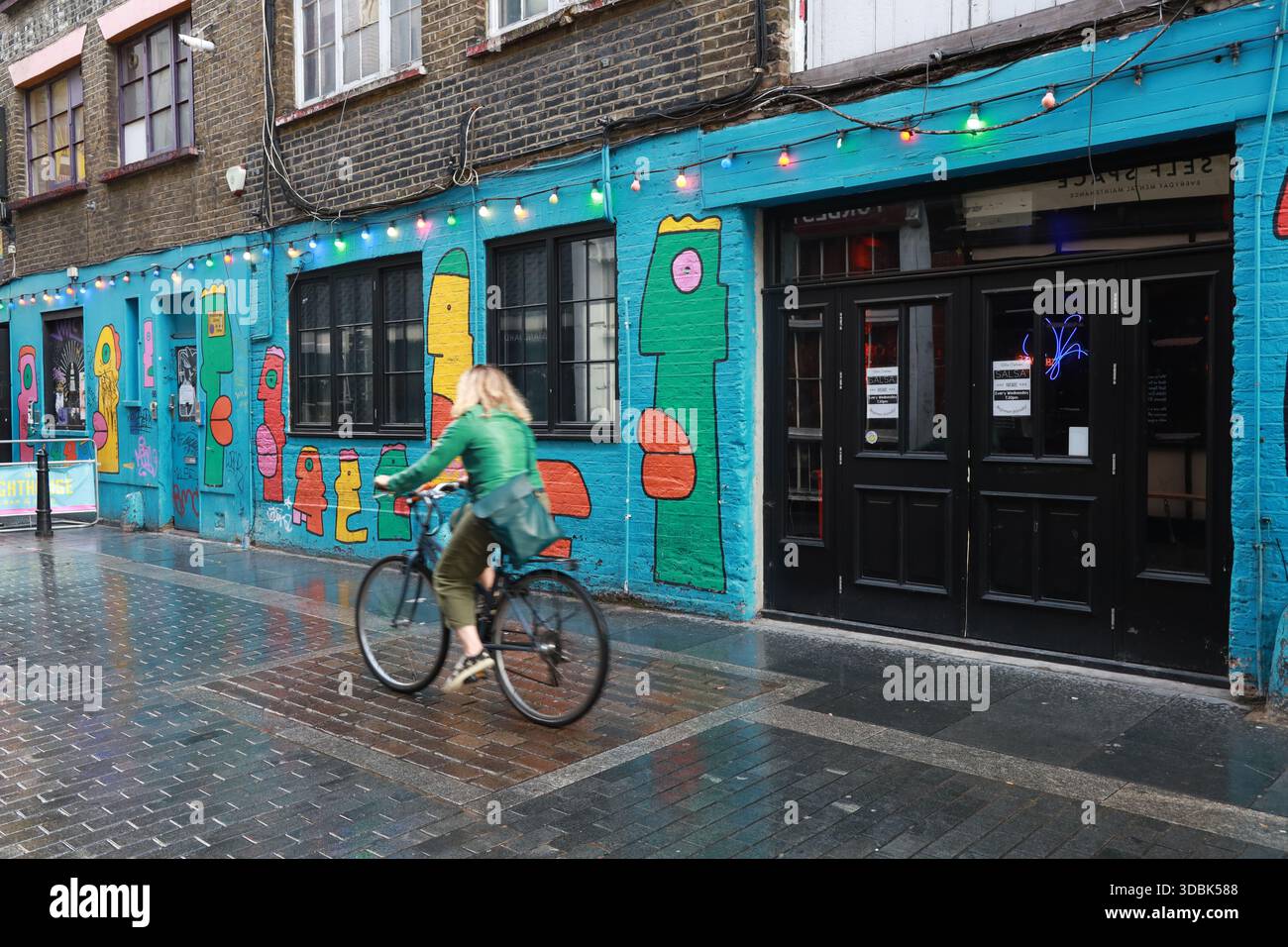 Radfahrer fahren an einem regnerischen Tag an Graffiti und Street Art im Shoreditch-Viertel im Osten Londons vorbei. Stockfoto