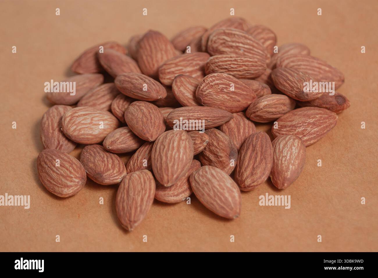 Mandeln liegen auf einem einfachen Blatt Papier auf und betonen ihre natürliche Textur in einer sauberen minimalen Szene. Stockfoto