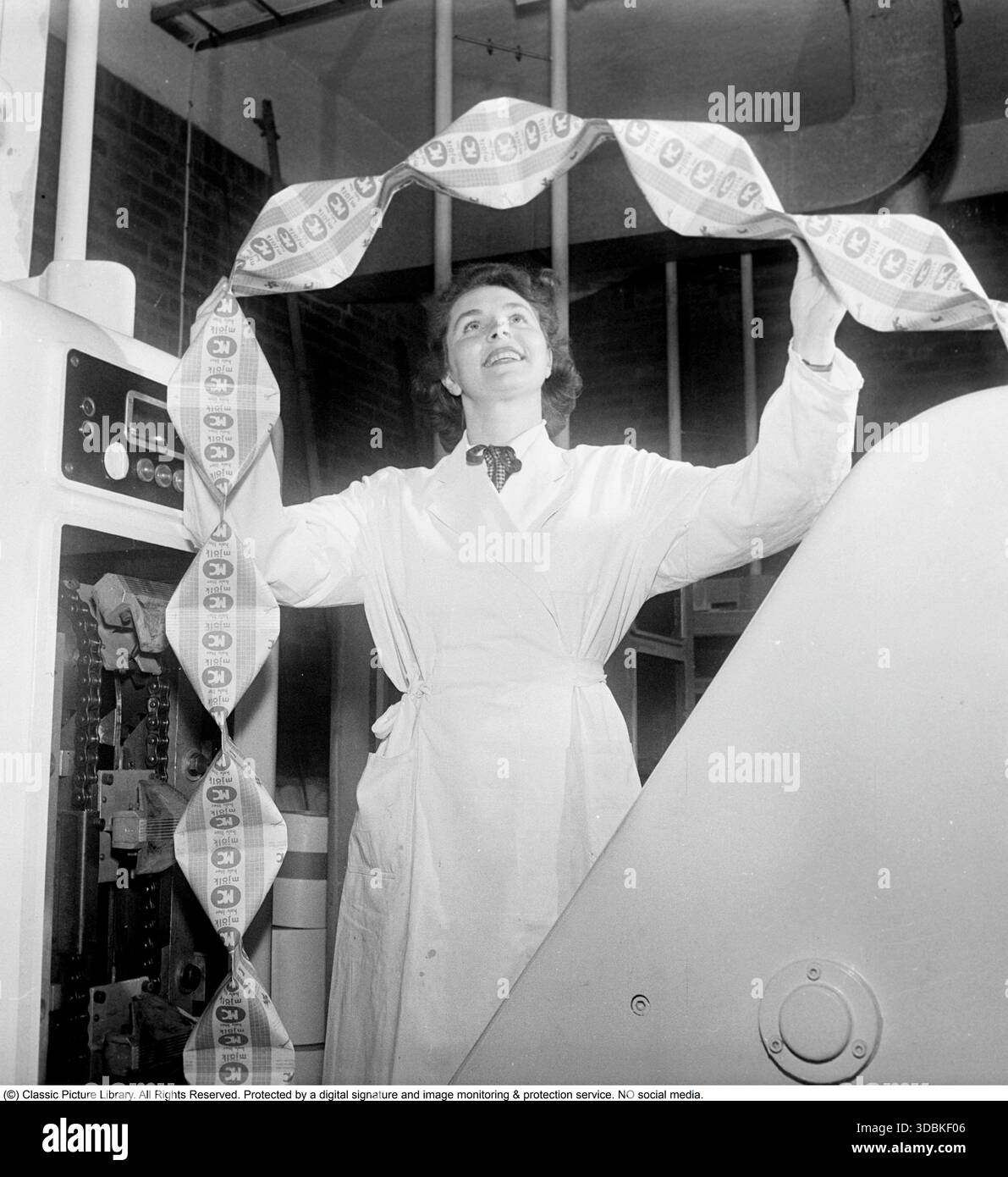 TETRA Pak Geschichte. 1951 präsentierte Tetra Pak seinen neuen Milchkarton in Form eines Tetraeders. Der Karton wurde aus einem Papier-Kunststoff-Laminat hergestellt, das zu einem Röhrchen gerollt wurde. Es wurde mit Milch gefüllt und dann in einer Maschine versiegelt, die die Enden rechtwinklig zusammendrückte, um die Pyramidenform zu bilden. Diese Packungen wurden als „tetra“ oder „Tetras“ bezeichnet. Dieser Karton wurde von Erik Wallenberg erfunden und von Ruben Rausing vermarktet und brachte das Tetra-Pak-Imperium ins Leben, das bald die Verpackung von flüssigen Lebensmitteln dominierte. Eine Mitarbeiterin an einer Maschine, die die fertigen Milchtetren noch in ungeschnittener Form in einem en produziert hat Stockfoto