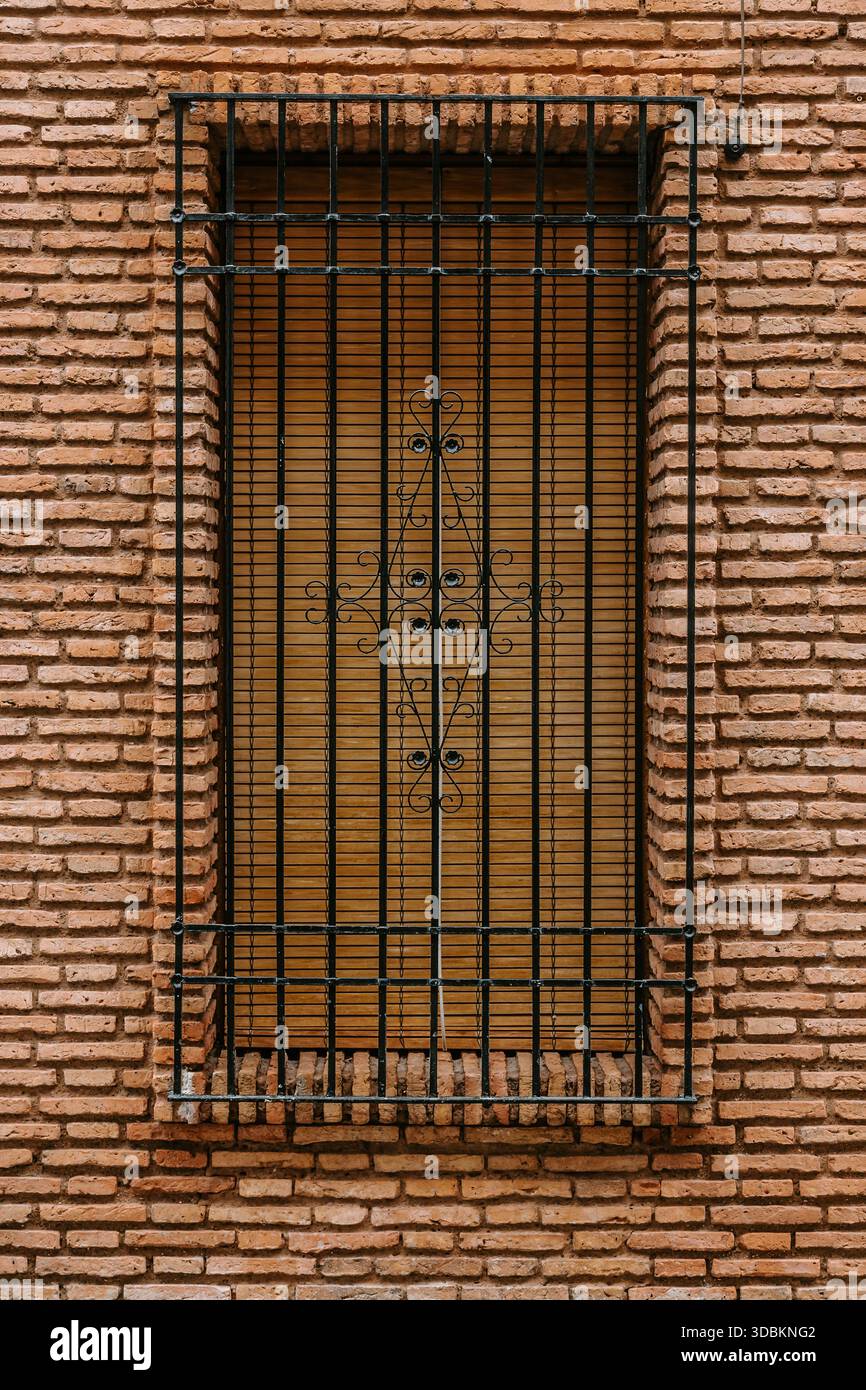 Fenster mit einem schützenden schmiedeeisernen Gitter und geschlossenen Holzjalousien an einer alten Ziegelmauer, die typische Architektur in Cordoba, Andalusien, Spai widerspiegelt Stockfoto