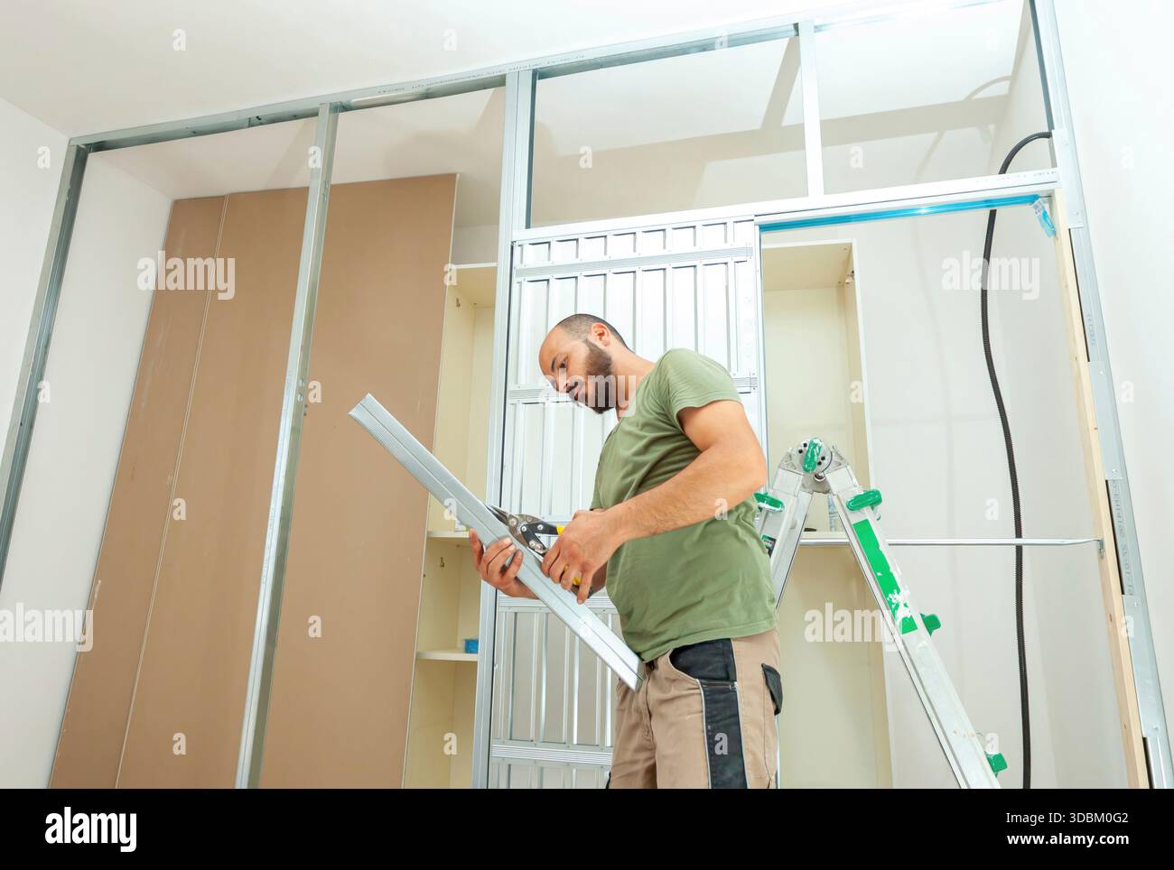 Handwerker schneiden Metallprofile für die Installation von Gipskartonwänden in einem Haus, das gerade renoviert wird, und verwenden Metallbolzen und -Schienen, um Präzision in Konstruktion und Design zu gewährleisten Stockfoto