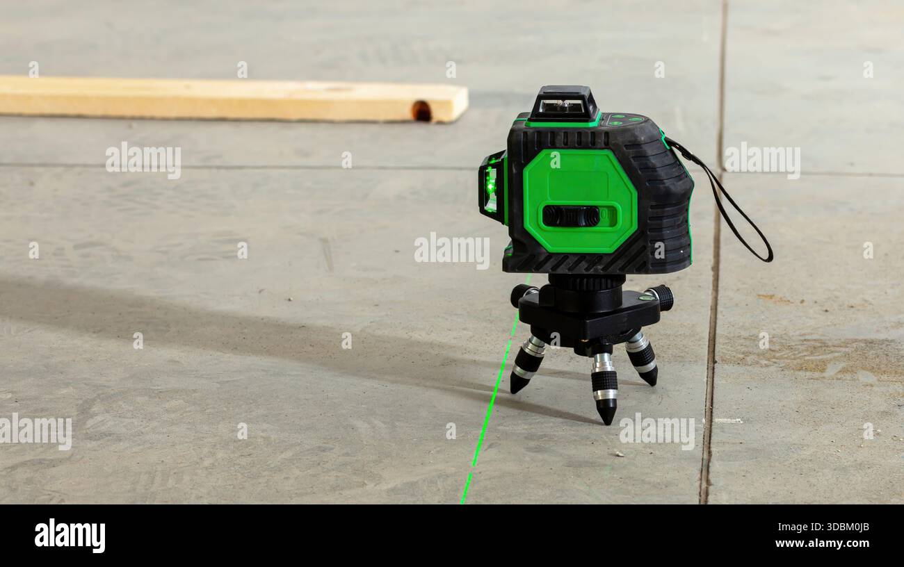 Grünes Laser-Nivellierwerkzeug, das während eines Renovierungsprojekts eine helle Linie auf einen Betonboden projiziert und so präzise Messungen und Ausrichtung gewährleistet Stockfoto