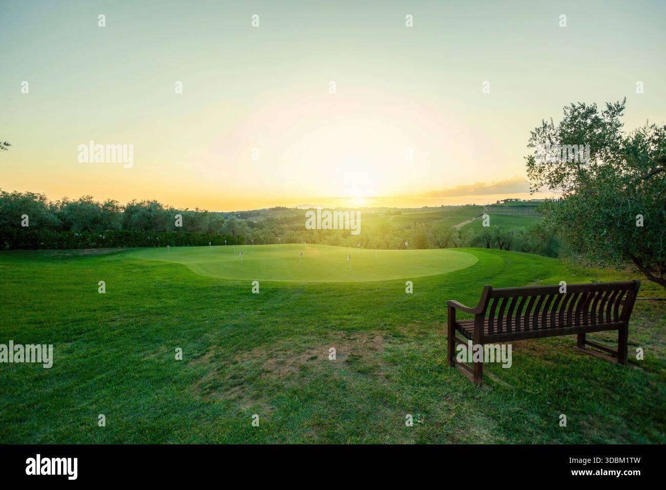 Holzbank mit Blick auf das Putting Green eines Golfplatzes bei Sonnenuntergang in der toskanischen Landschaft, italien Stockfoto