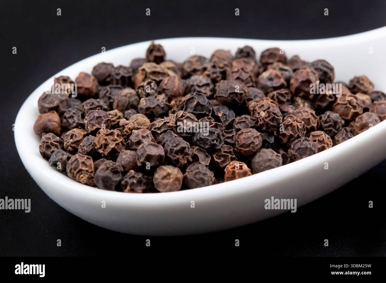 Pfefferkörner in weißen Löffel am schwarzen Tisch Stockfoto
