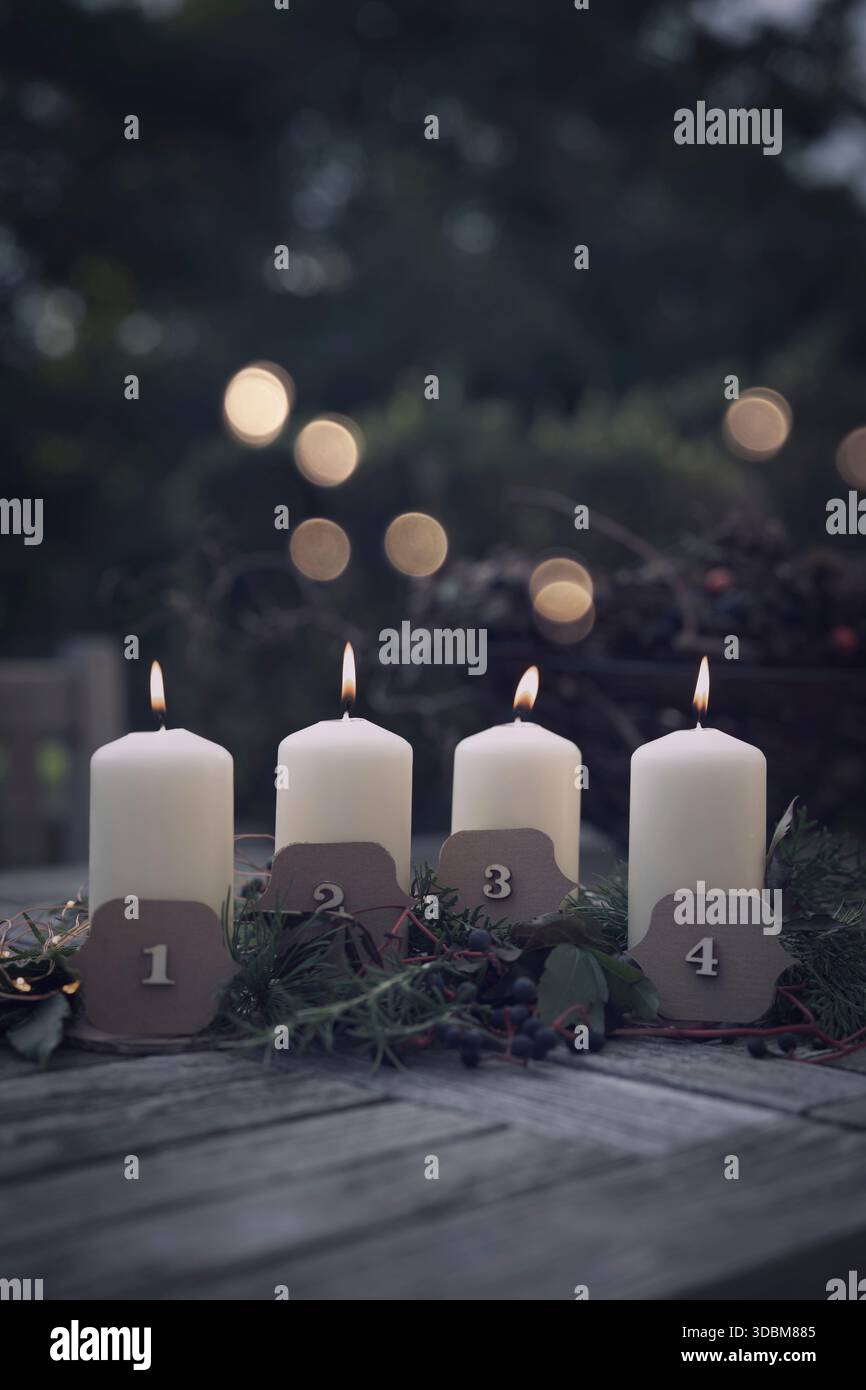 Brennende Adventskerzen mit weihnachtsdekoration und goldenem Bokeh auf einer Terrasse in der Abenddämmerung. Vertikaler weihnachtshintergrund mit Platz für Text. Stockfoto