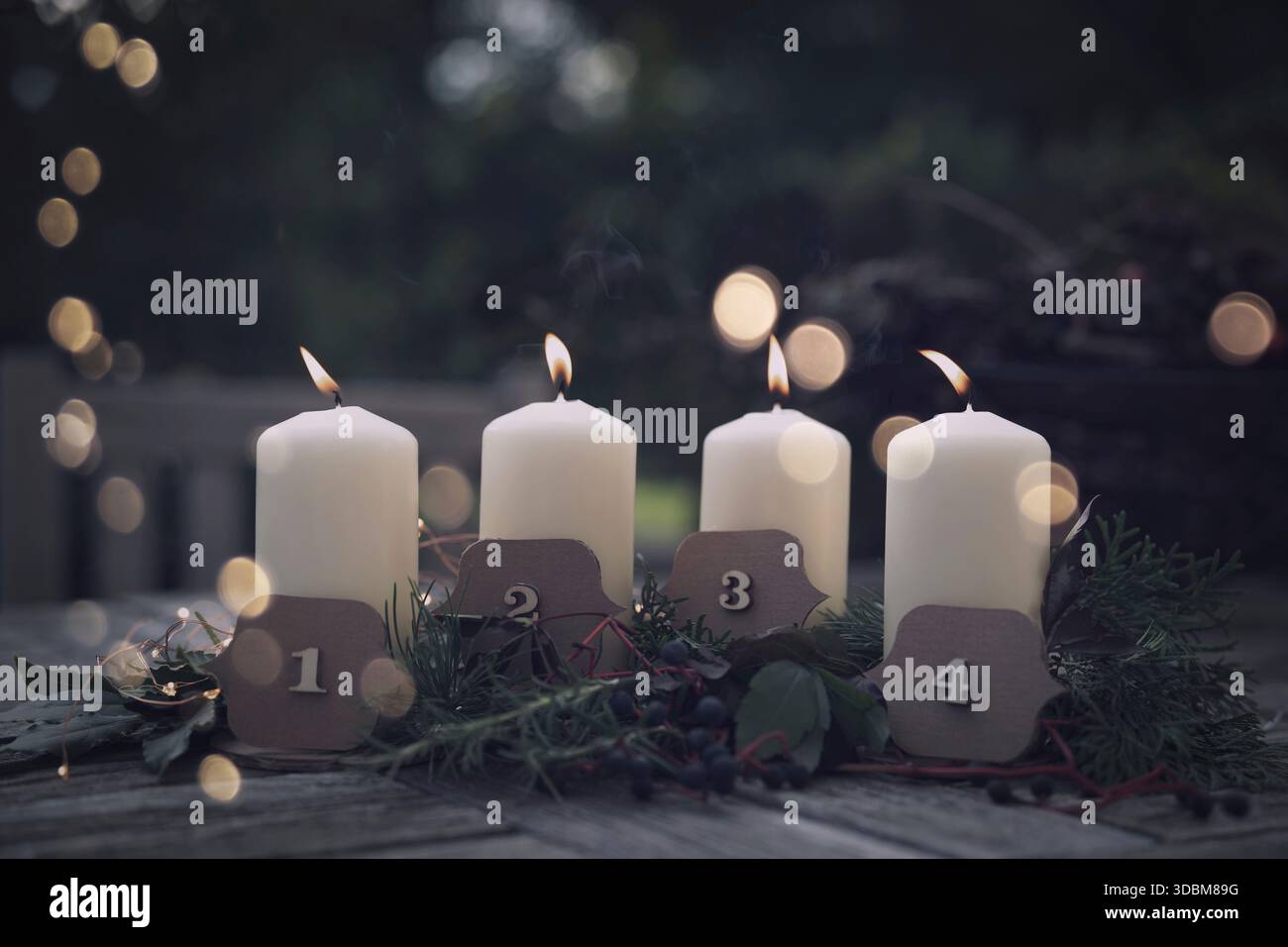 Brennende Adventskerzen mit weihnachtsdekoration und goldenem Bokeh auf einer Terrasse in der Abenddämmerung. Weihnachtshintergrund mit Platz für Text. Stockfoto