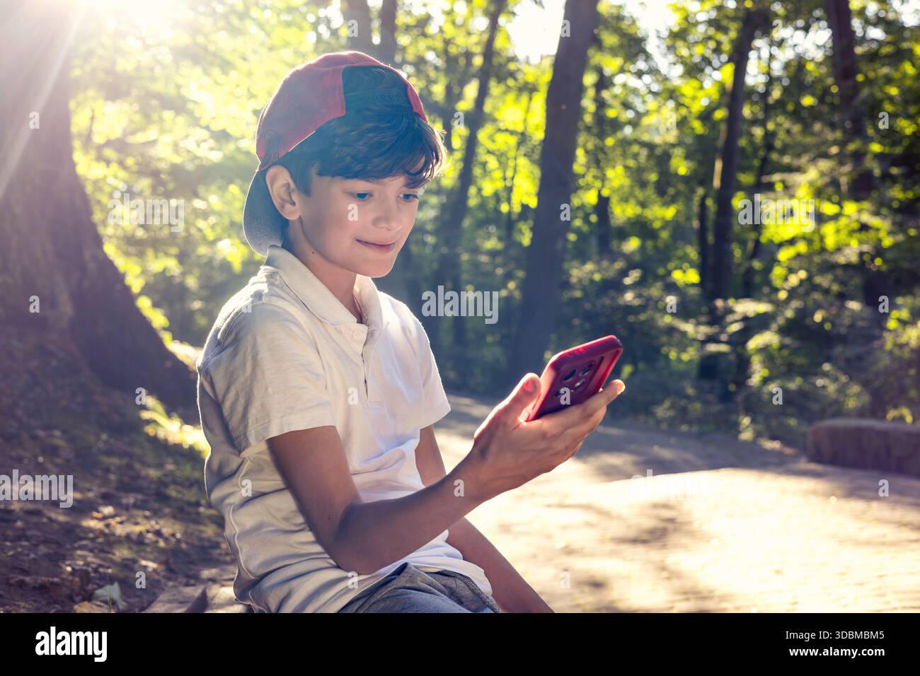 Kind mit Smartphone im Park, Junge mit Mobiltelefon im Freien, digitale Kindheit, Bildschirmzeit, Technologieabhängigkeit, Kinder und Gadgets, soziale Medien, Stockfoto
