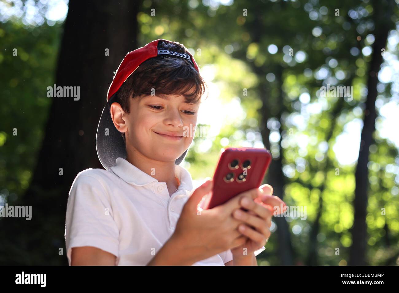 Kind mit Smartphone im Park, Junge mit Mobiltelefon im Freien, digitale Kindheit, Bildschirmzeit, Technologieabhängigkeit, Kinder und Gadgets, soziale Medien, Stockfoto