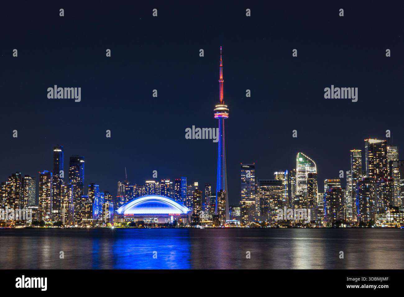 Der CN Tower und das Rogers Centre aus der Vogelperspektive leuchten hell vor dem Nachthimmel und spiegeln sich in den ruhigen Gewässern von Toronto, Ontario, Kanada. Stockfoto