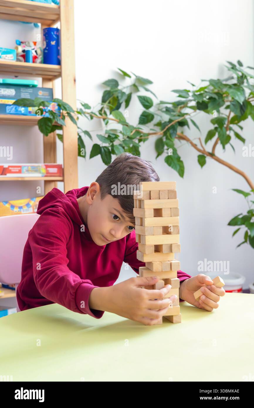 Junge spielt Jenga in einem gemütlichen Kinderzimmer. Das Thema kognitive Entwicklung, logisches Denken, motorische Fähigkeiten, psychische Gesundheit, autistische Unterstützung Stockfoto