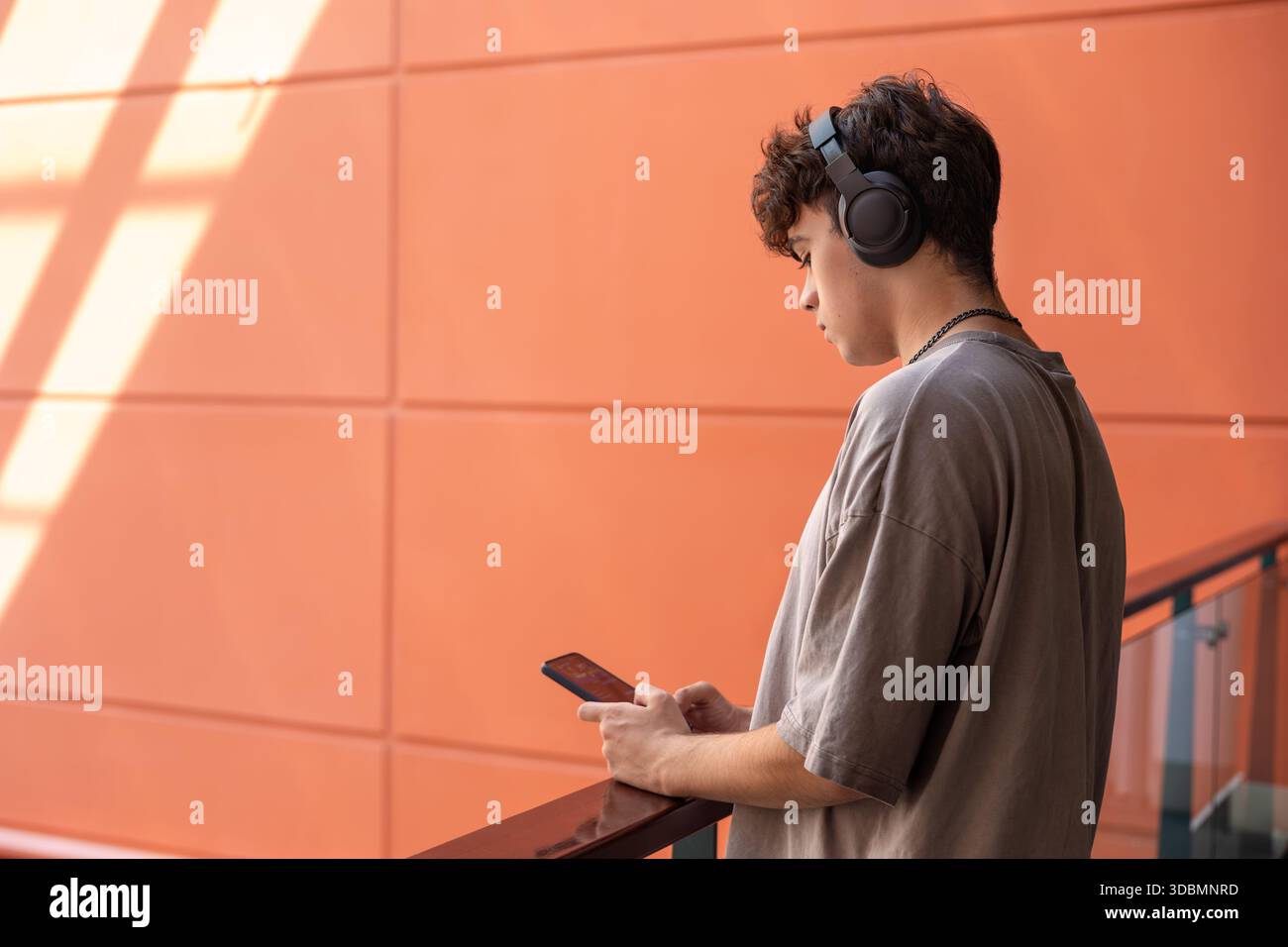 Teenager mit Kopfhörern und Blick auf Smartphone, modernen Jugendstil, Technologieabhängigkeit, soziale Medien, Online-Kommunikation, Emotionen, Stress, Mu Stockfoto