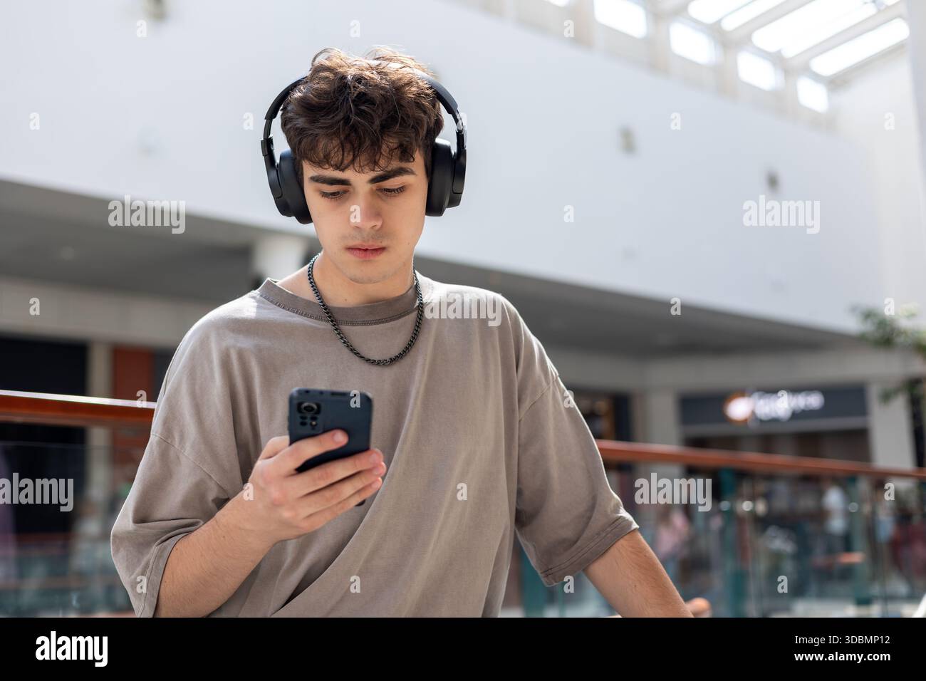 Teenager mit Kopfhörern und Blick auf Smartphone, modernen Jugendstil, Technologieabhängigkeit, soziale Medien, Online-Kommunikation, Emotionen, Stress Stockfoto