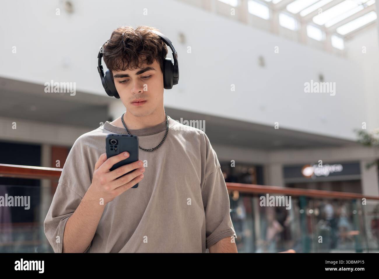 Teenager mit Kopfhörern und Blick auf Smartphone, modernen Jugendstil, Technologieabhängigkeit, soziale Medien, Online-Kommunikation, Emotionen, Stress Stockfoto