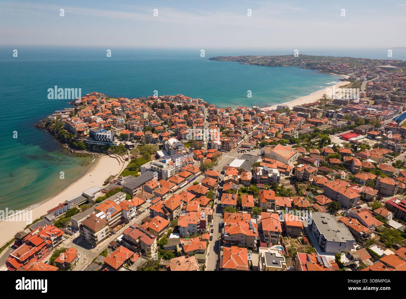 Blick aus der Vogelperspektive auf die rot gekachelten Dächer stürzen sich in Richtung des türkisfarbenen Meeres und treffen auf Sandstrände in einem pulsierenden Küstenpanorama, Sozopol, Burgas, Bulgarien. Stockfoto