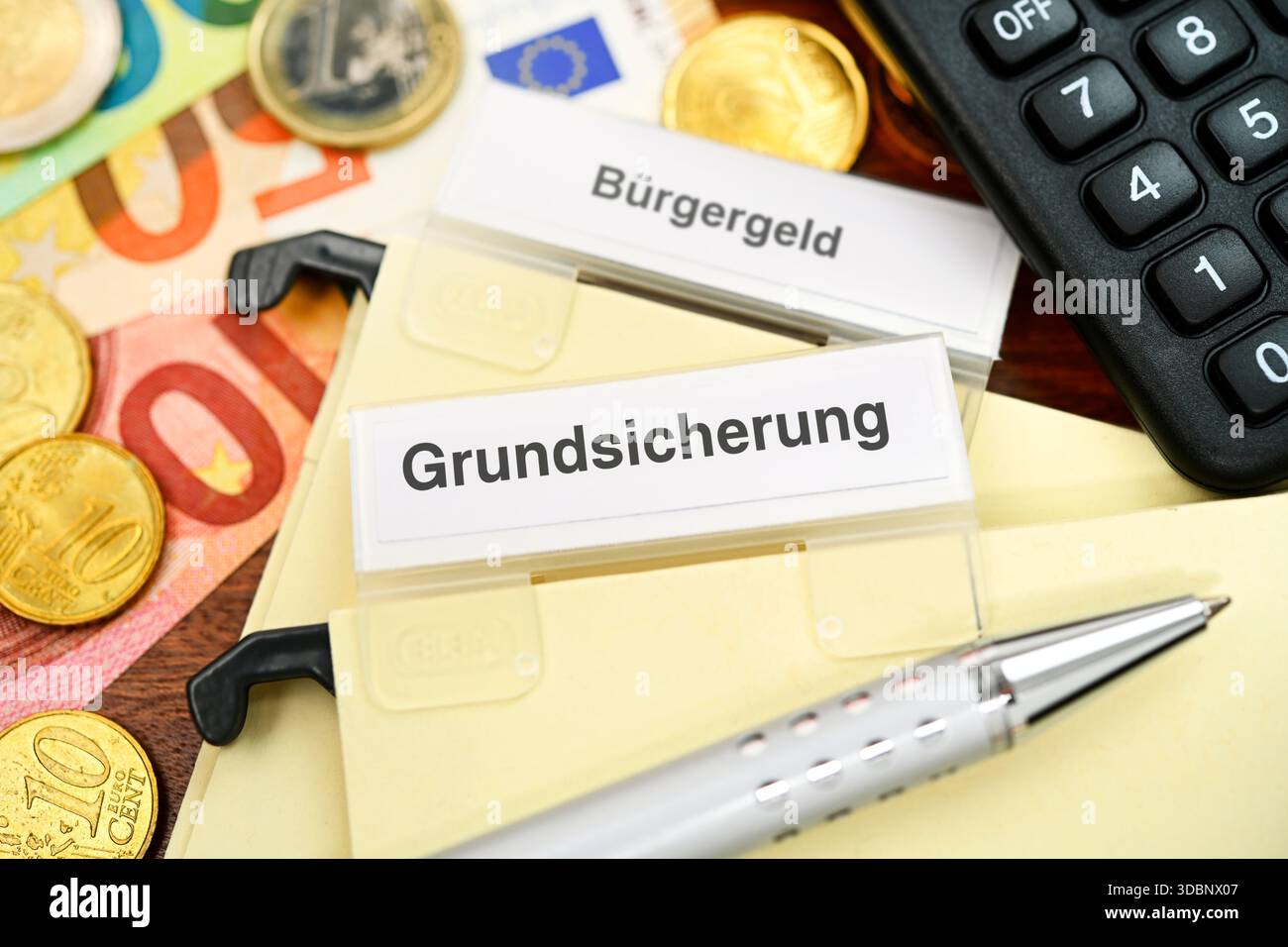 Ordner mit der Aufschrift Grundsicherung und Bürgergeld mit Münzen und Banknoten auf einem Schreibtisch Stockfoto